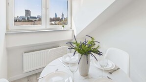 Ein Essbereich mit Tisch für zwei Personen, einer Zimmerpflanze und Blick auf eine Stadtlandschaft durch ein Fenster.