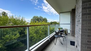 A balcony with a glass railing, a table with chairs, and a potted plant.