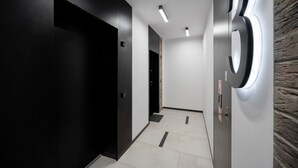 A modern hallway with a black door, a wall-mounted elevator, and a tiled floor.