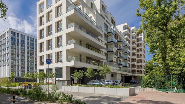 A modern multi-story residential building with balconies, a bike parking sign, and a gated entrance.
