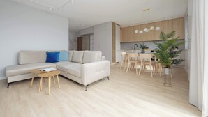 A modern living room with a sofa, coffee table, and dining area with chairs and a plant. - Comfortable Apartment for 6 Persons | Parking | Balcony (Warszawa)