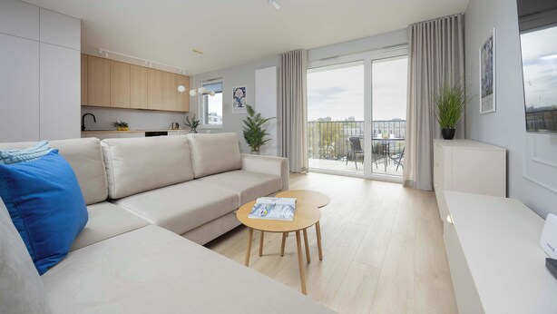 A modern living room with a sofa, a coffee table, and a view of the city through large windows. - Comfortable Apartment for 6 Persons | Parking | Balcony (Warszawa)