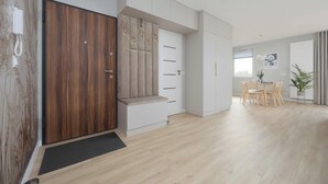 A modern living room with a wooden door, a bench, a dining area with a table and chairs, and a potted plant. - Comfortable Apartment for 6 Persons | Parking | Balcony (Warszawa)