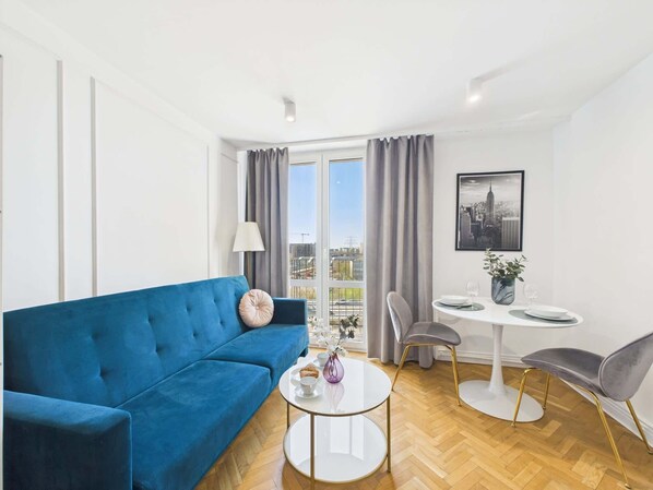 A modern living room with a blue sofa, a round coffee table, and a dining area with a white table and chairs.
