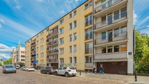 Un edificio residencial de varios pisos con balcones, una calle empedrada con ladrillos y coches estacionados.