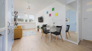 Una cocina moderna con comedor, armarios blancos, una mesa pequeña con sillas y un televisor montado en la pared.