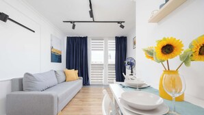 A modern living room with a grey sofa, a dining table with plates and a glass, and a yellow vase with sunflowers.