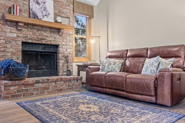 A living room with a brick fireplace, leather sofa, and a patterned rug. - Spacious Well Appointed Retreat Minutes from Excelsior, Lake Minnetonka & More (Chanhassen)