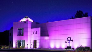 Un edificio moderno con un techo de forma piramidal único, iluminado con luces púrpuras, y un llamativo símbolo de ancla en la fachada.