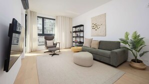 Un salon moderne avec un canapé gris, une table basse ronde, un fauteuil gris, un téléviseur à écran plat, une bibliothèque et une plante en pot.