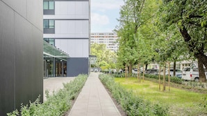 Un chemin bordé de verdure et une façade de bâtiment moderne.
