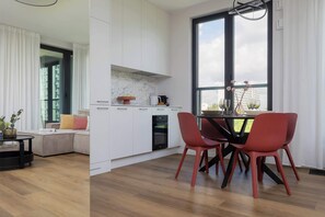 A modern kitchen with white cabinetry, a dining area with red chairs, and a large window offering a view of the city. - Stylish Apartment in the Center | Balcony | Parking | Smart TV (Warszawa)