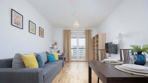 Una sala de estar moderna con un sofá gris, una mesa de comedor para dos personas y un televisor en la pared.