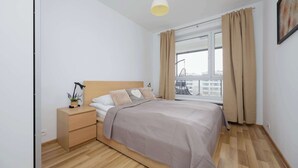 Un dormitorio con una cama, una mesita de noche, una lámpara y una ventana con cortinas.