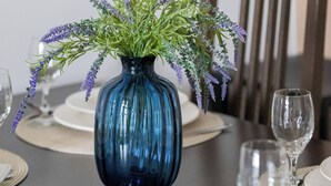 Una mesa de comedor preparada con platos, cubiertos y un jarrón con flores.