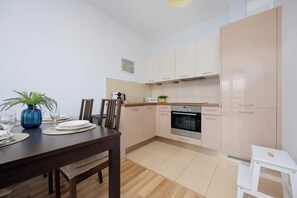 Una cocina moderna con armarios de colores claros, horno empotrado y comedor con mesa y sillas de madera.