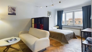 Una camera d'albergo con un divano, un letto, un tavolino, una libreria e una finestra con tende.