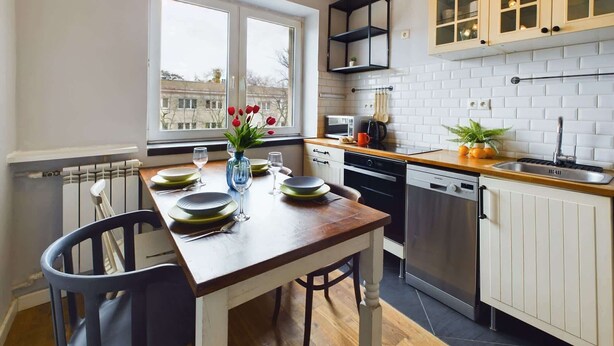 Una cucina moderna con mobili bianchi, un tavolo da pranzo in legno e una finestra con vista sulla città.