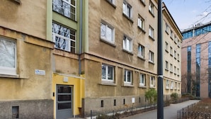 Un edificio a più piani con una porta gialla e finestre, un'insegna che indica un ufficio di sorveglianza, e un vialetto lastricato con una recinzione metallica.