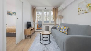 Un salon moderne avec un canapé gris, une table basse ronde en bois et un téléviseur posé sur un meuble en bois.
