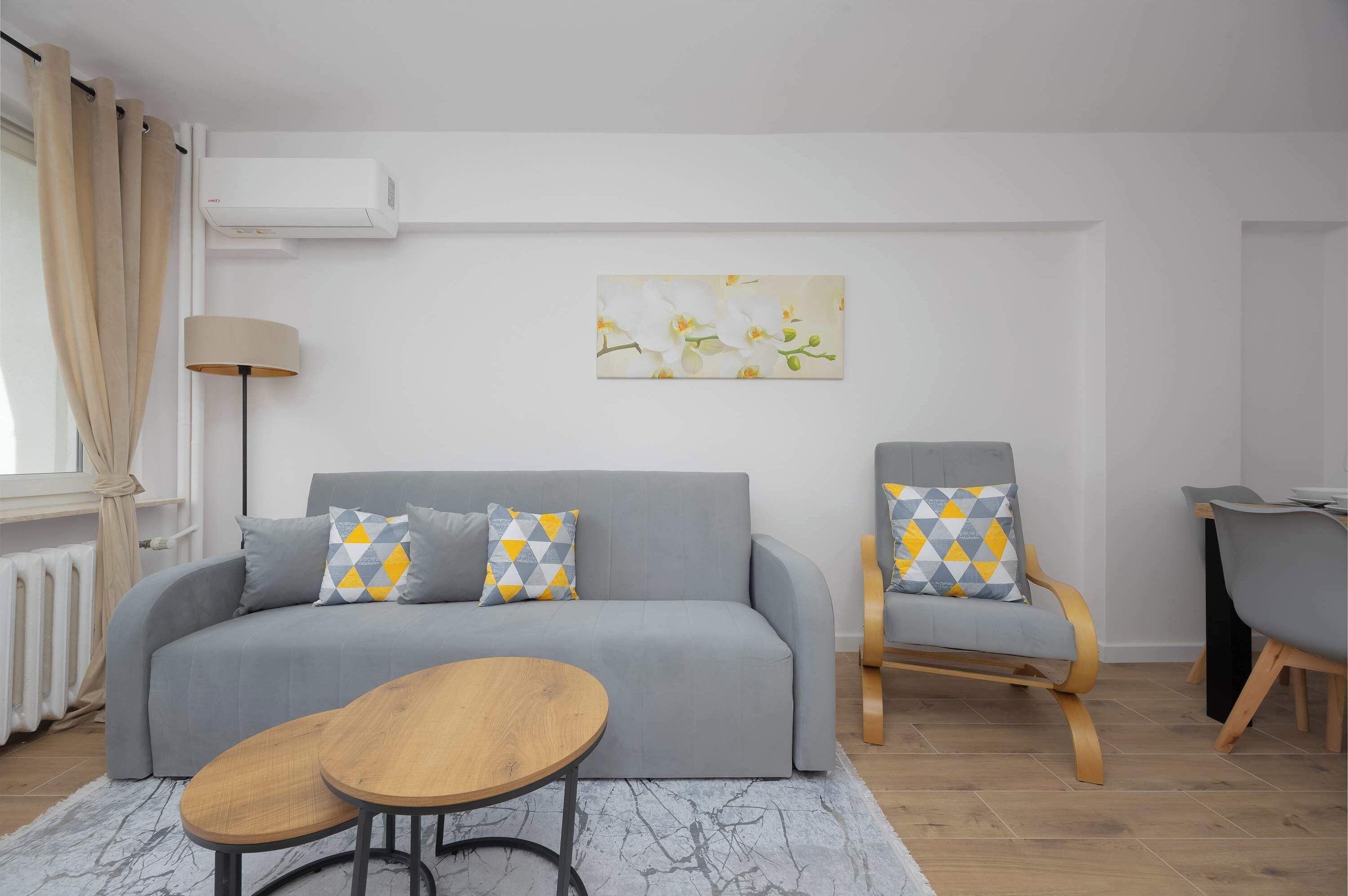 A modern living room with a grey sofa, two armchairs, a wooden coffee table, and a painting of flowers on the wall.