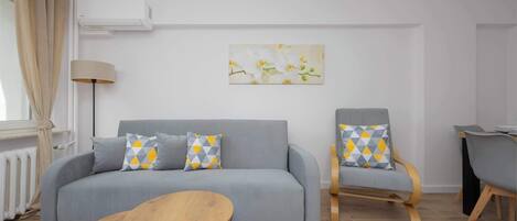 A modern living room with a grey sofa, two armchairs, a wooden coffee table, and a painting of flowers on the wall.