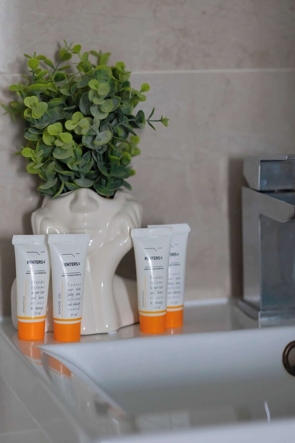 A bathroom with a white sink, three toiletries tubes, and a green plant in a white vase.