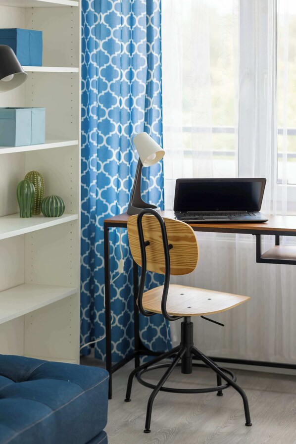 Un espacio de oficina moderno con un escritorio de madera, una computadora portátil, una silla y una cortina azul estampada.