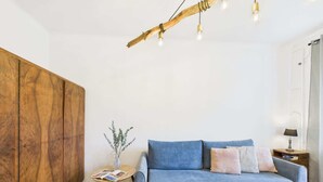 Una sala de estar moderna con un sofá azul, piso de madera en espiga, un armario de madera y una lámpara colgante.