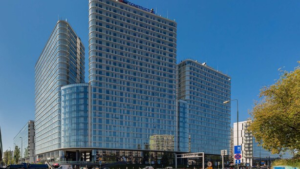 A modern high-rise hotel with a glass facade, multiple floors, and a prominent 'CONSTRUCTION' sign at the top. - Elegant Studio in Wola | Air Conditioning and Balcony (Warszawa)