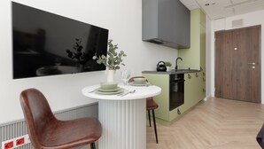 A modern kitchen with a white table set for two, a large flat-screen TV, and a green cabinet. - Stylish Studio with Air Conditioning | Close to EXPO XXI (Warszawa)