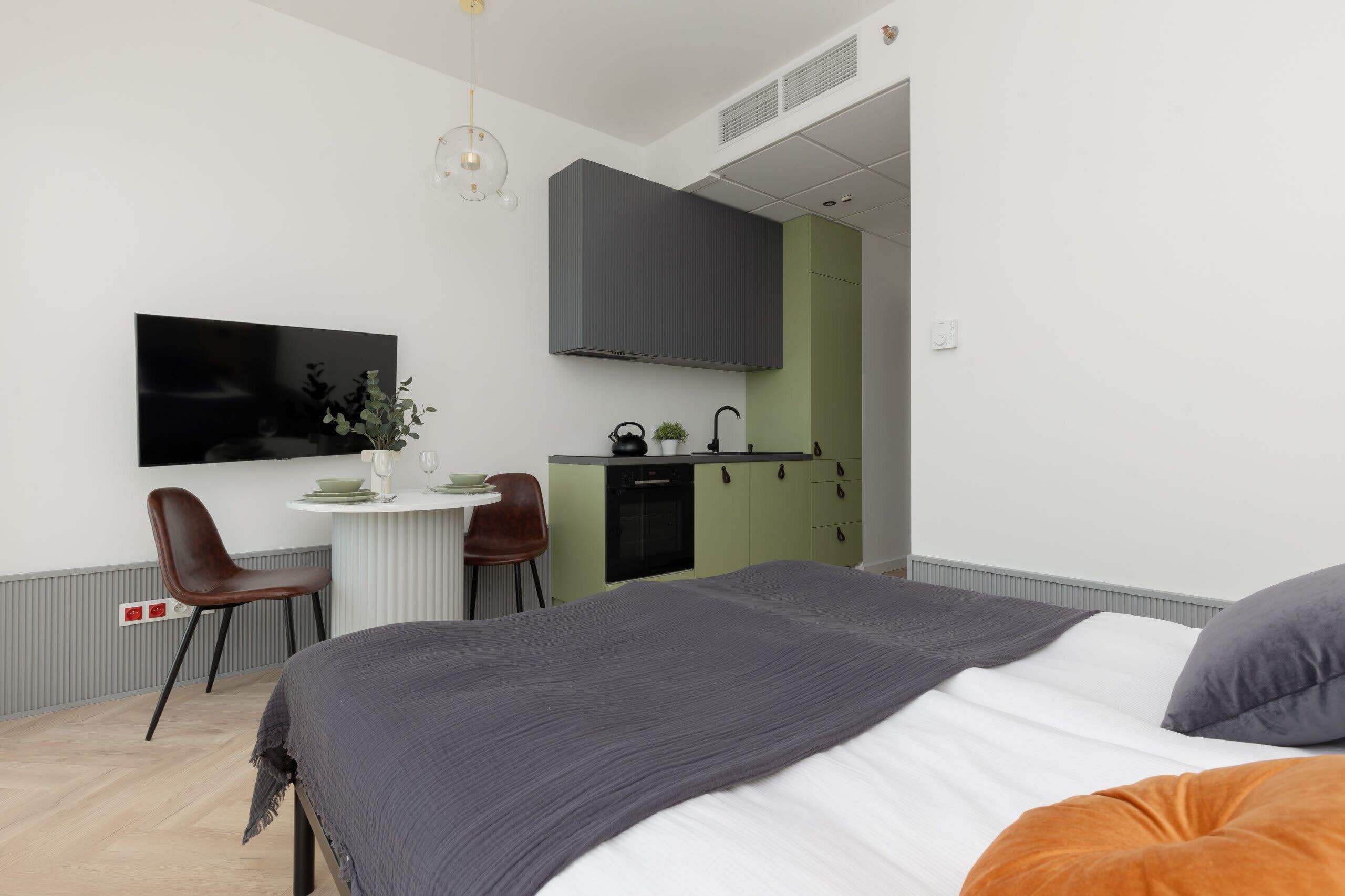 Un dormitorio moderno con una cama grande, un escritorio con silla, un televisor y una kitchenette.