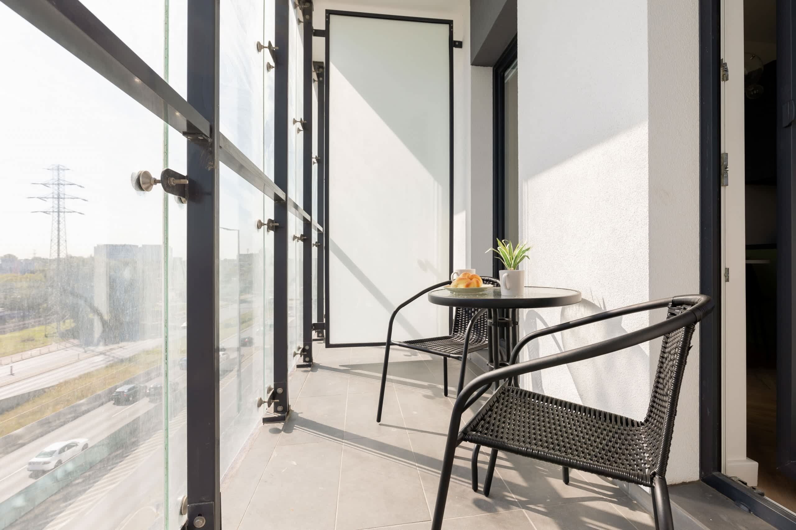 Ein Balkon mit Glastür, einem kleinen Tisch mit Stühlen und einem Blumentopf.