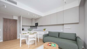 Ein modernes Wohnzimmer mit einem grünen Sofa, einem Holztisch und einem Essbereich mit weißen Stühlen und einem kleinen Tisch.