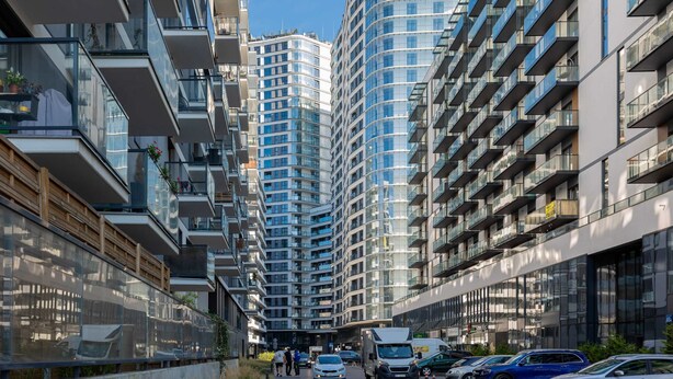 Eine moderne Stadtstraße mit Hochhäusern, einem Fußgängerweg und geparkten Autos.