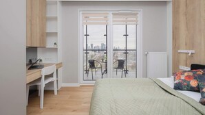 Ein Schlafzimmer mit Bett, Schreibtisch, Laptop, Stuhl und einem Balkon mit Sitzgelegenheiten.