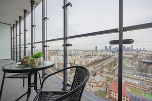A balcony with a table and chairs, a potted plant, and a city view.
