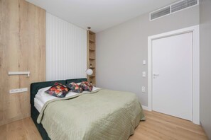 A bedroom with a bed, a wooden wardrobe, a white door, and a shelf unit.