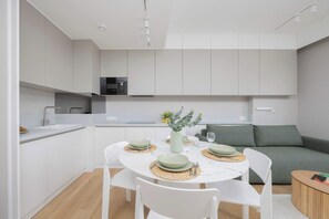 A modern kitchen with white cabinets, a dining table set with green plates and white chairs, and a green sofa in the background.