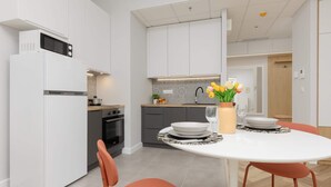 A modern kitchen with white cabinets, a built-in microwave, and a dining area with a round table and orange chairs.