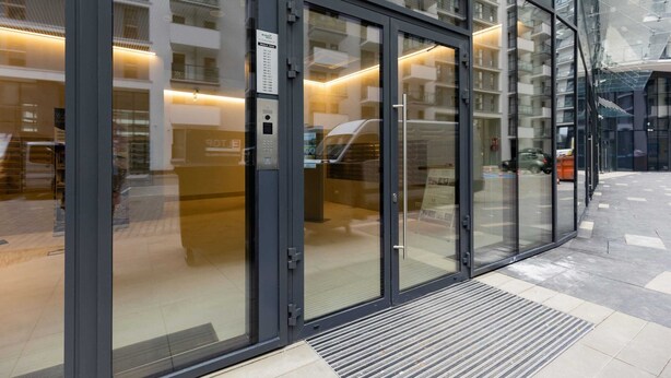 A modern building entrance with glass doors, a digital display, and a tiled floor.