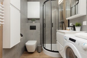 Ein modernes Badezimmer mit einer gläsernen Duschkabine, Toilette, Waschmaschine und einem Schrank mit einer Pflanze.