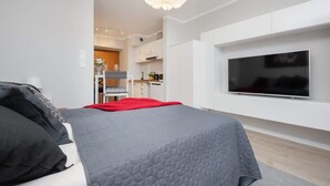Ein modernes Schlafzimmer mit einem großen Bett, einem an der Wand montierten Fernseher und einer Küchenzeile im Hintergrund.