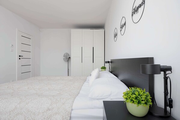 A bedroom with a bed, a bedside table with a lamp, a potted plant, and a wall with three circular signs.