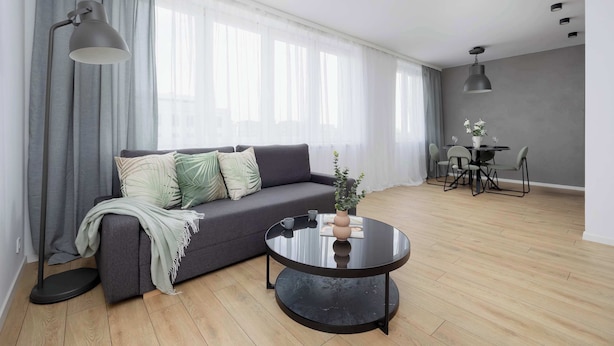 Una sala de estar moderna con un sofá gris, una mesa de centro negra redonda y una zona de comedor con mesa y sillas.