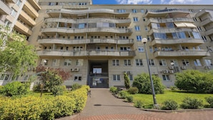 Un edificio residencial de varios pisos con balcones, una entrada central y un sendero pavimentado que conduce a ella.