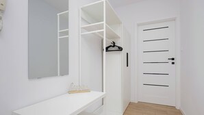 Una habitación blanca con suelo de madera, un escritorio blanco, un armario blanco y una puerta blanca con pomo negro.