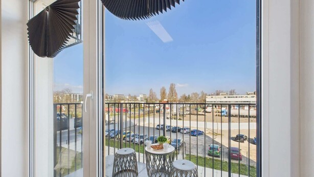 Un balcon donnant sur un parking et des immeubles.