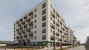 Un immeuble résidentiel moderne à plusieurs étages, doté de balcons, d’une entrée au niveau du sol et d’une grue de construction visible en arrière-plan.