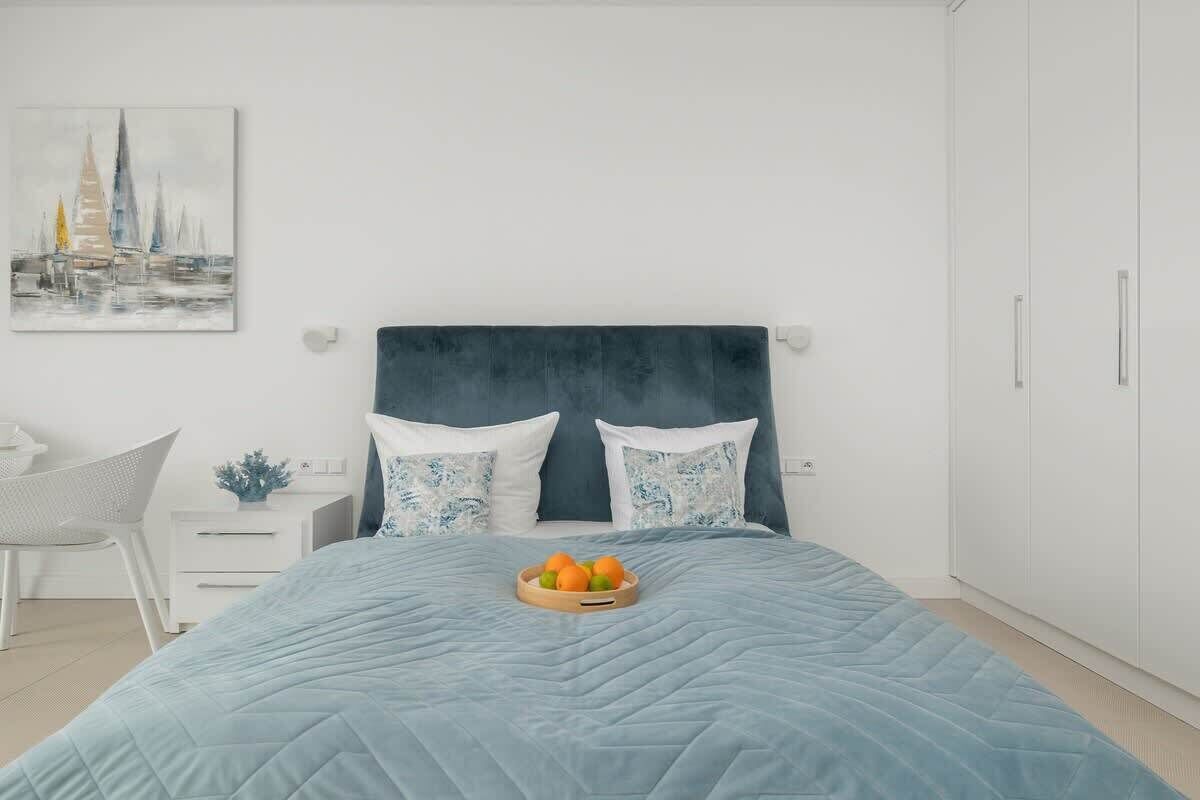 Une chambre à coucher comprenant un lit, une table de chevet, une chaise et une œuvre d’art accrochée au mur.